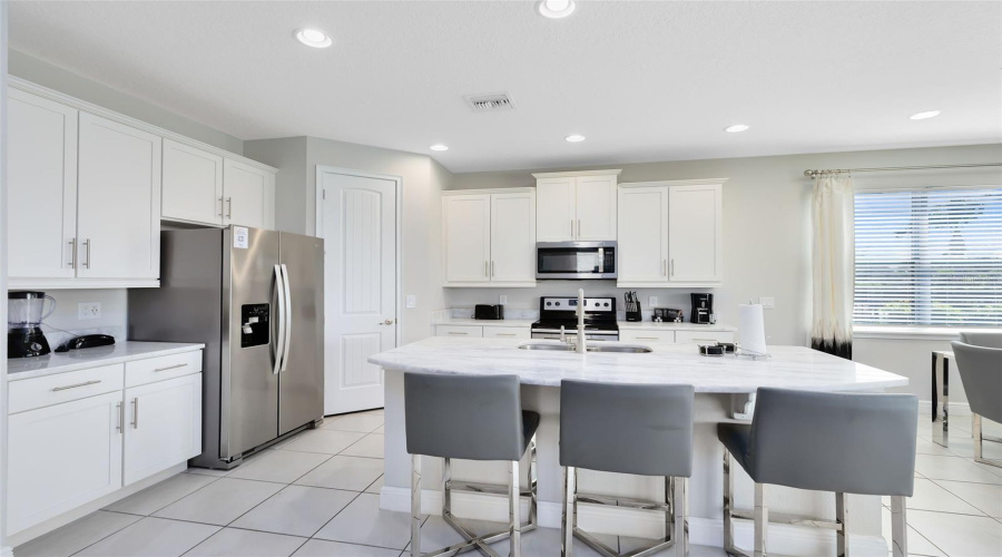 The beautiful and open kitchen is equipped with stone countertops, solid wood cabinets, stainless steel appliances, an island, a breakfast bar, an eat-in area, and all the kitchen essentials you will need for your family and future guests.