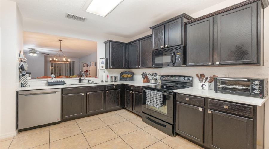 Tiled Kitchen Features White Quartz Counters And Breakfast Bar, Modern Black Appliances And Stainless Steel Dishwasher And Bay Window With Large Dinette Eating Space.