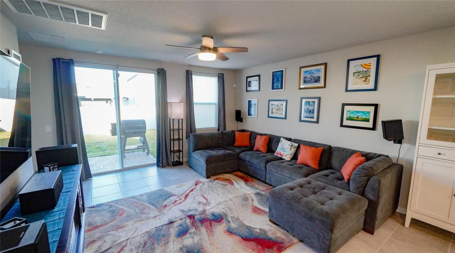 The Spacious Living Room Features A Ceiling Fan And Oversized Sliding Doors Accessing The Fenced In Backyard!