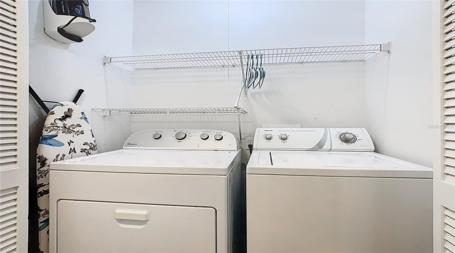 Laundry closet with washer, dryer, shelving, ironing board & iron.