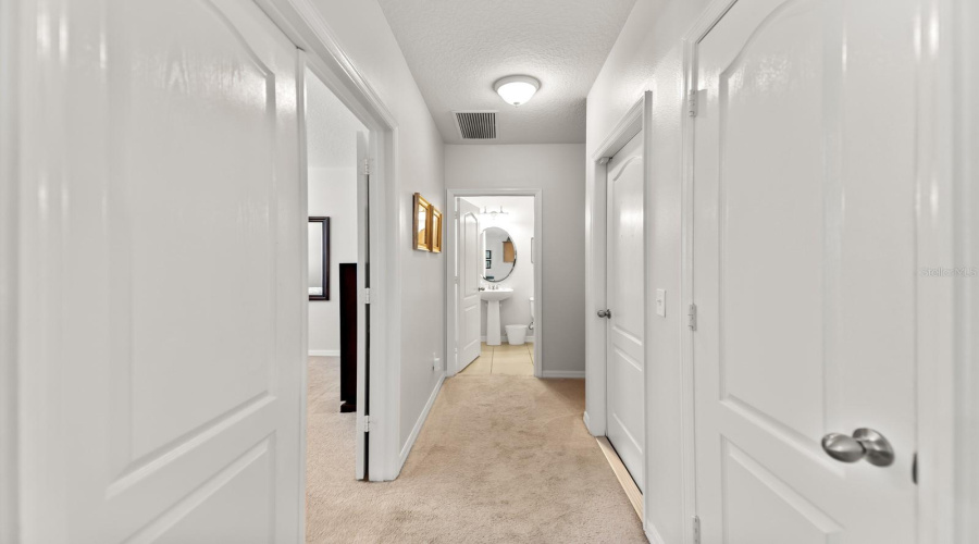 Corridor Leading From Family Room To The Downstairs Primary Bedrooms Suite, Garage, Half Bathroom And Understairs Storage Area