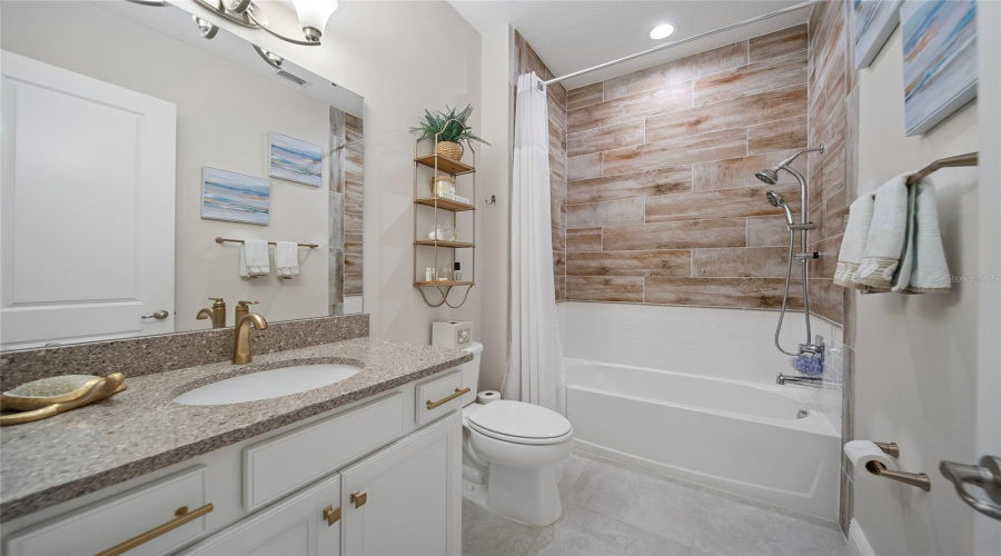 Warm wood-look tile and gold accents give this guest bath a cozy, elevated feel.