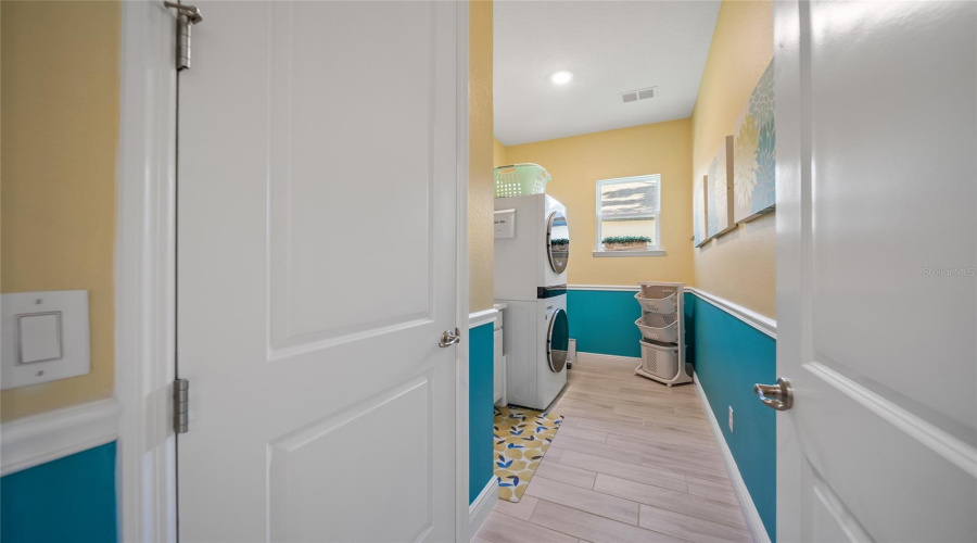 Bright and cheerful laundry room with stacked washer-dryer, sink, and plenty of space to fold.