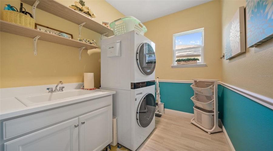 Bright and cheerful laundry room with stacked washer-dryer, sink, and plenty of space to fold.