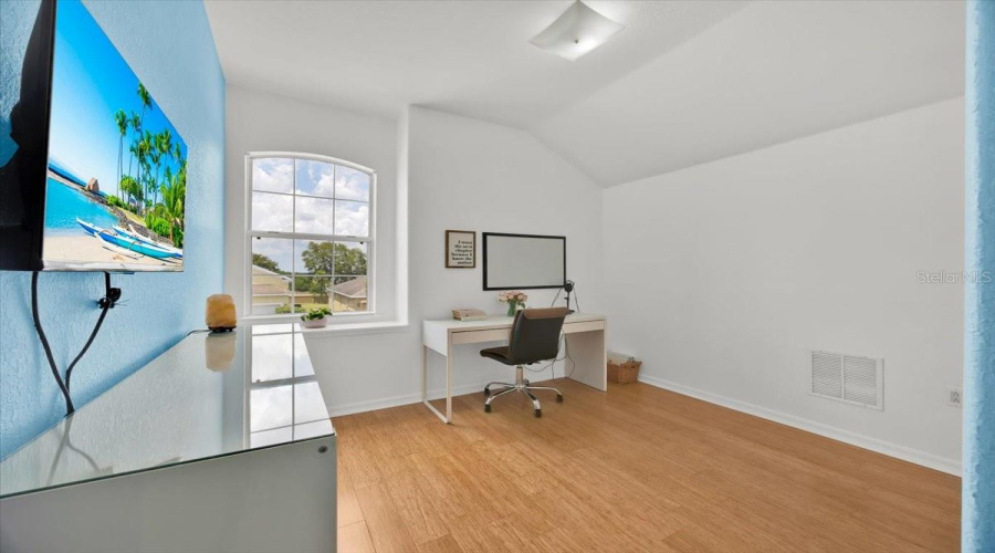 This bright upstairs bedroom, currently styled as a TikTok content office, features an arched window with a lovely view of the quiet street and charming front garden. Natural light pours in, creating a serene workspace complemented by updated bamboo-style flooring found throughout the home.Español:Este luminoso dormitorio en la planta alta, actualmente utilizado como oficina para crear contenido de TikTok, cuenta con una ventana arqueada que ofrece una encantadora vista de la calle tranquila y el jardín delantero. La luz natural llena el espacio, creando un ambiente sereno que se complementa con el suelo tipo bambú recientemente actualizado que se extiende por toda la casa.