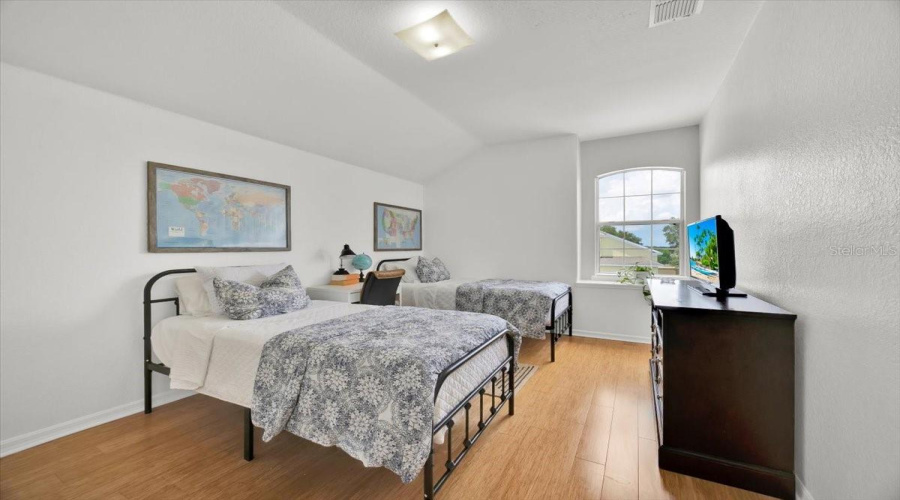 This spacious upstairs bedroom features a serene view of the quiet street and front garden through the arched window. Enjoy the warmth and durability of updated bamboo-style flooring, along with a generous walk-in closet.Español:Este amplio dormitorio en la planta alta ofrece una vista tranquila hacia la calle y el jardín delantero a través de la ventana arqueada. Disfruta de la calidez y durabilidad del suelo tipo bambú, junto con un vestidor espacioso.