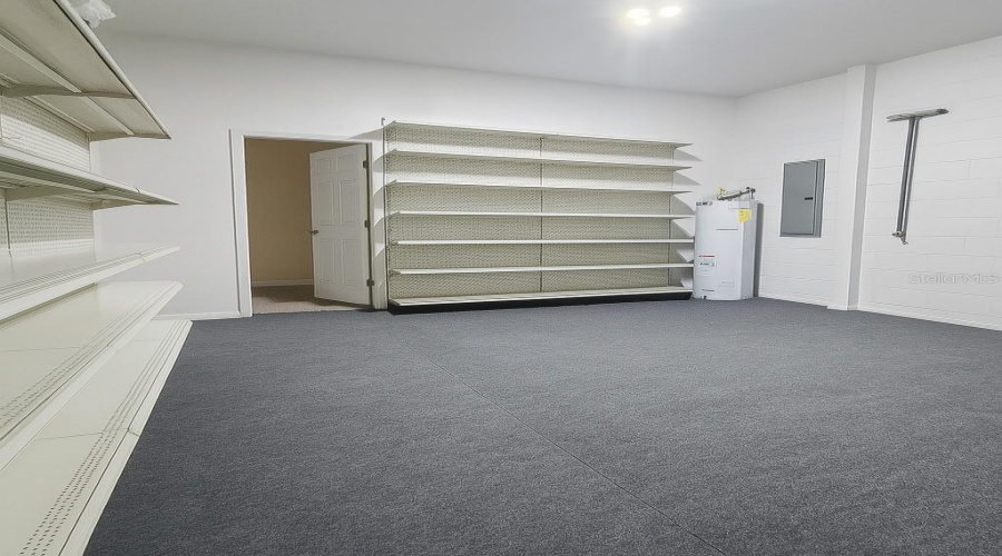 Spacious two-car garage featuring extensive built-in shelving on two walls—perfect for organized storage of tools, seasonal items, and more. The open layout offers plenty of room for vehicles while maintaining functionality and easy access to stored items. Grey carpet flooring and bright lighting make this garage both practical and inviting.Spanish:Amplio garaje para dos autos con estanterías integradas en dos paredes, ideal para mantener herramientas, artículos de temporada y mucho más perfectamente organizados. El diseño abierto ofrece espacio suficiente para los vehículos sin sacrificar funcionalidad ni accesibilidad. Piso con una alfombra gris e iluminación brillante lo hacen práctico y acogedor.