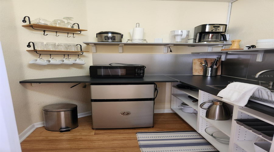 Cozy Kitchenette in Airbnb SuiteDiscover this beautifully organized kitchenette designed for efficiency and guest comfort. Features include sleek countertops, a compact stainless-steel fridge, microwave, and a deep stainless sink with modern faucet. Open shelving and warm bamboo floors used in homeowner's rental suite—ideal for guest suites, in-law quarters.
