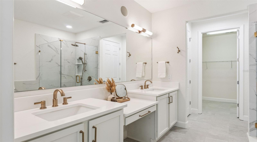 Luxurious master bath with dual vanities, quartz countertops, frameless glass shower, and large walk-in closet access.