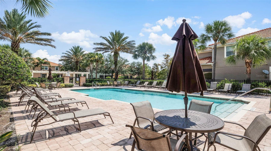 Resort-style pool with spacious sundeck, plenty of lounge seating, and shaded tables.