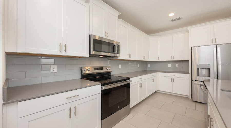 The designer Kitchen anchors the space with 42-inch white cabinetry, QUARTZ COUNTERTOPS, a generous breakfast bar, stainless steel appliances, a closet pantry, and a chic tile backsplash—ideal for hosting, gathering, and culinary creativity.