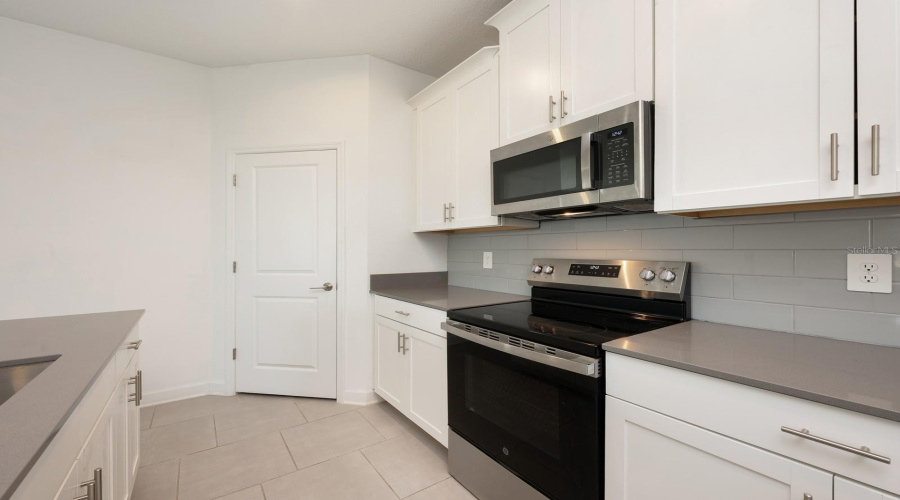 The designer Kitchen anchors the space with 42-inch white cabinetry, QUARTZ COUNTERTOPS, a generous breakfast bar, stainless steel appliances, a closet pantry, and a chic tile backsplash—ideal for hosting, gathering, and culinary creativity.