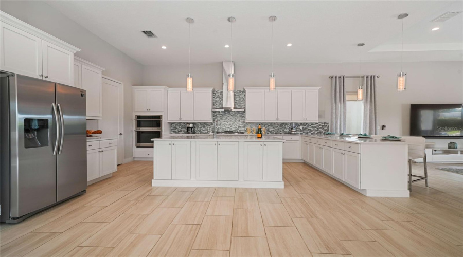The chef’s kitchen featuring a gas cooktop with exterior-vented hood, built-in oven and microwave, refrigerator, dishwasher, and an expansive center island with generous seating.