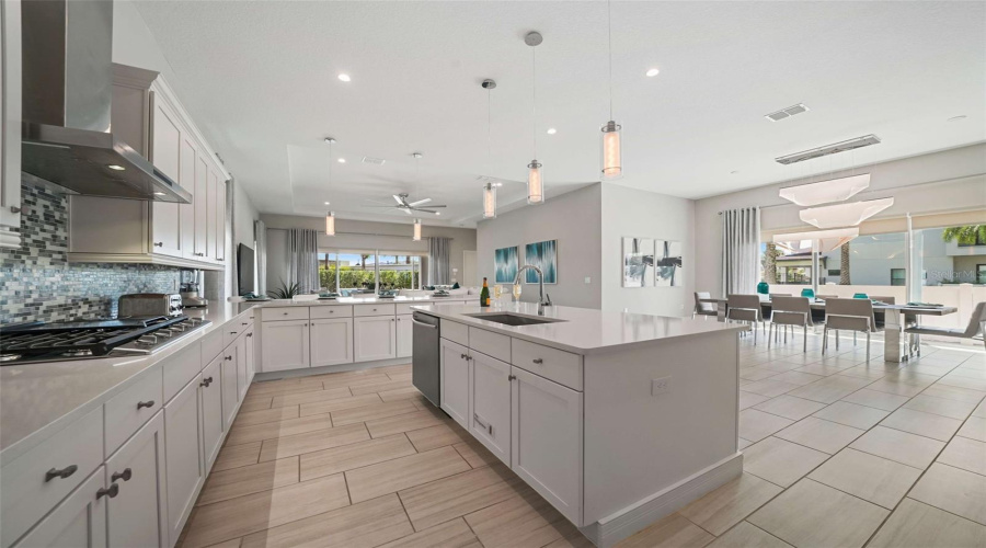 The chef’s kitchen featuring a gas cooktop with exterior-vented hood, built-in oven and microwave, refrigerator, dishwasher, and an expansive center island with generous seating.