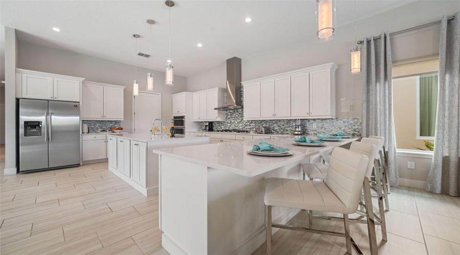 The chef’s kitchen featuring a gas cooktop with exterior-vented hood, built-in oven and microwave, refrigerator, dishwasher, and an expansive center island with generous seating.