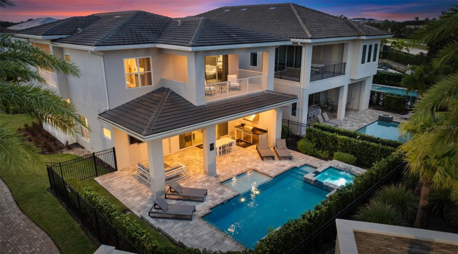 This resort-style backyard is a private oasis with a heated custom pool, raised spa, paver deck, lush landscaping, and striking fire bowls. A covered lanai with a summer kitchen and outdoor TV, plus a second-story balcony overlooking the pool, create the perfect setting for relaxation and entertaining from day to night.