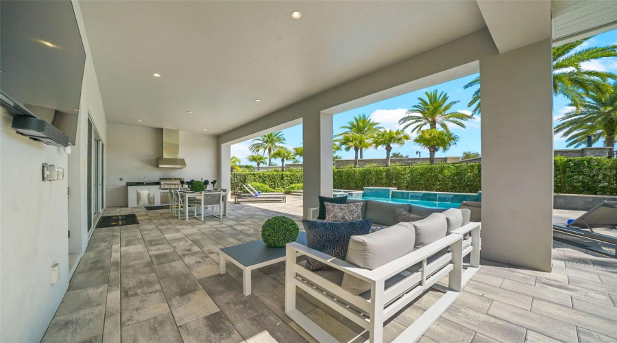 his resort-style backyard is a private oasis with a heated custom pool, raised spa, paver deck, lush landscaping, and striking fire bowls. A covered lanai with a summer kitchen and outdoor TV, plus a second-story balcony overlooking the pool, create the perfect setting for relaxation and entertaining from day to night.