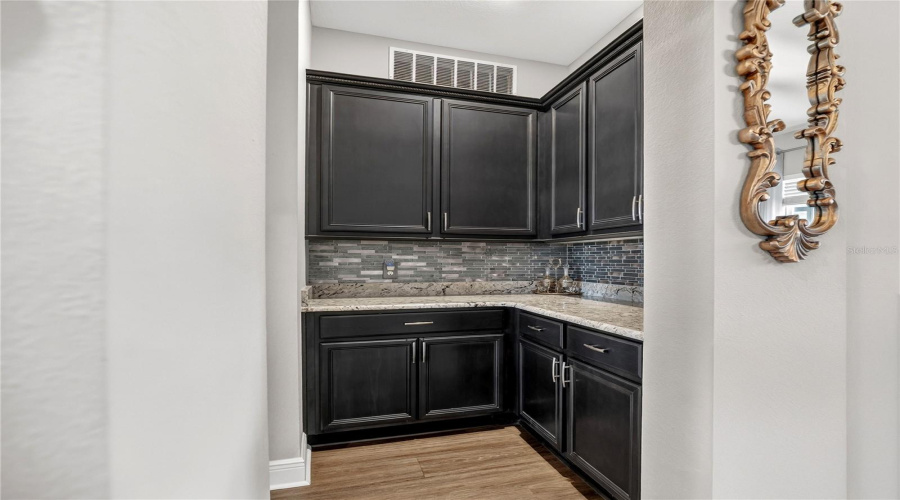 Secondary prep area with custom cabinetry, stone counters, and tile backsplash.