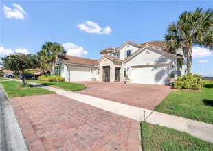 Wide brick-paver driveway and Mediterranean-style exterior with mature landscaping.