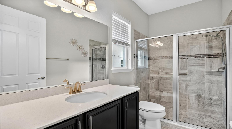 Pool bath with single-sink vanity, stone counters, and glass-enclosed shower.