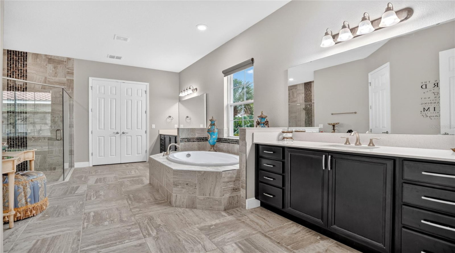 Alternate view of the primary bathroom with soaking tub, dual vanities, and stone finishes.