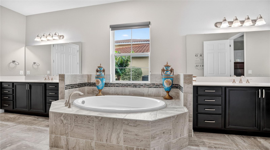 Primary bathroom with soaking tub, dual vanities, and tile surround.