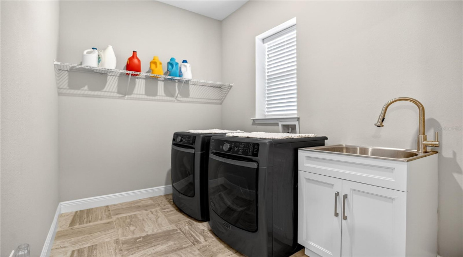 Dedicated laundry room with washer and dryer, utility sink, and storage shelving.