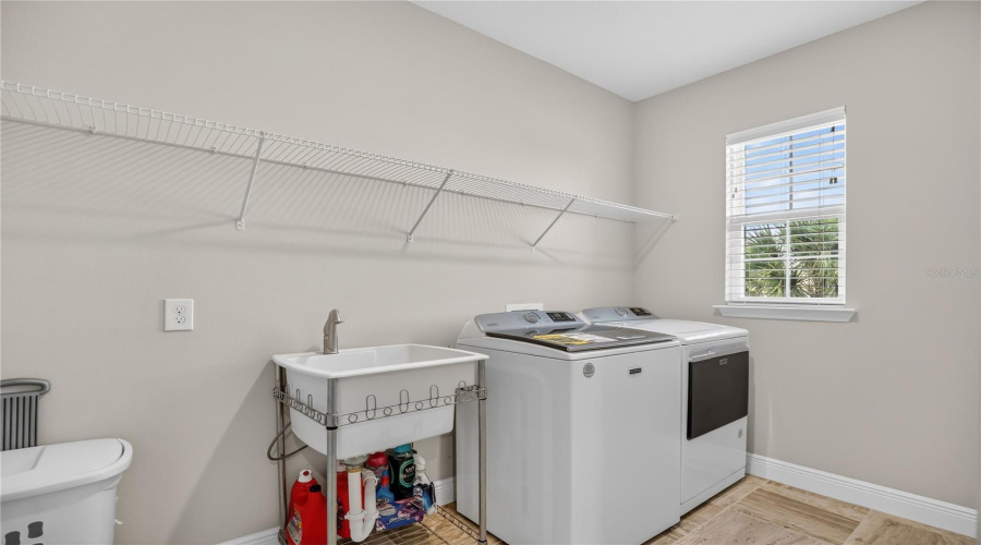 Upstairs laundry room with sink, storage shelving, and natural light.