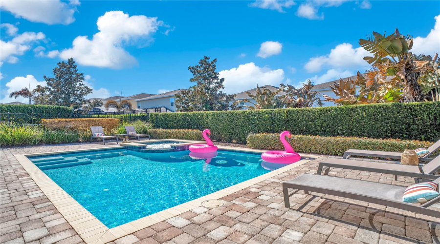Private heated pool with brick paver deck, lush landscaping, and ample space for lounging and entertaining