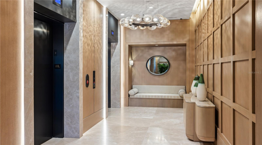 Elegant, hotel-inspired elevator lobby featuring warm wood paneling, integrated ambient lighting, polished stone floors and controlled-access elevators. A thoughtfully designed seating area adds a refined, welcoming touch.