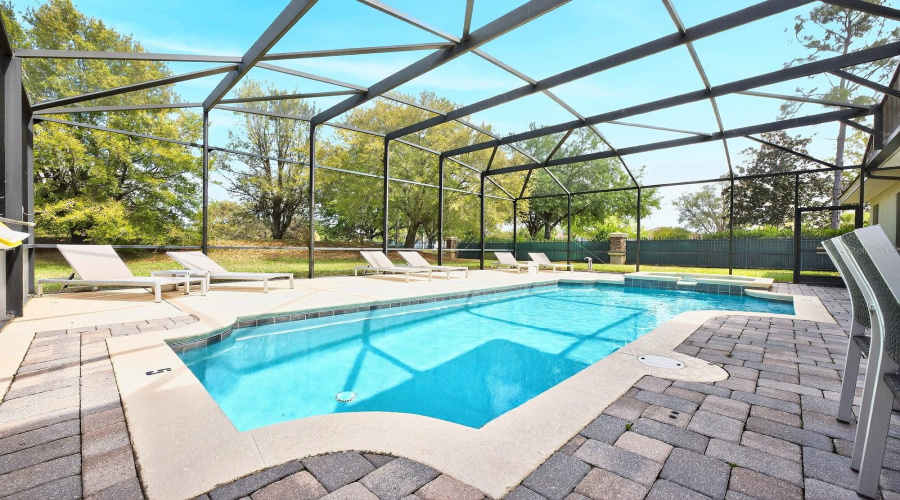 Outdoor living shines with a SCREENED HEATED POOL & SPA, a COVERED LANAI, and an extended PAVER PATIO overlooking the spacious backyard framed by mature trees – perfect for relaxing evenings or entertaining guests.
