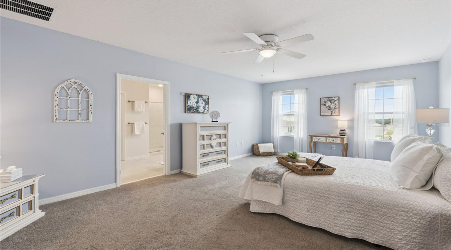 View of owners bedroom and bathroom highlighting the natural light from the front windows and ceiling fan