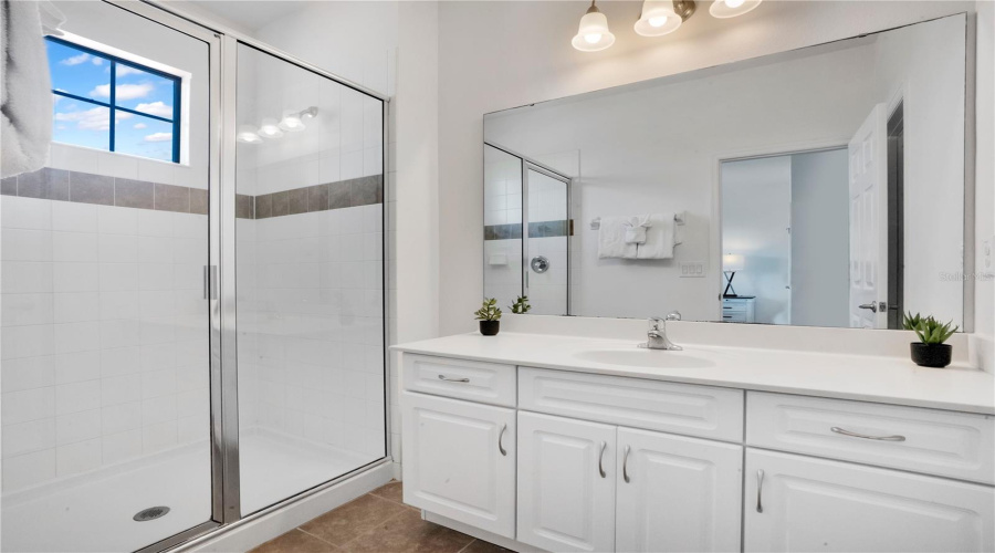 Bathroom with dual vanity, large mirror, and walk in shower.