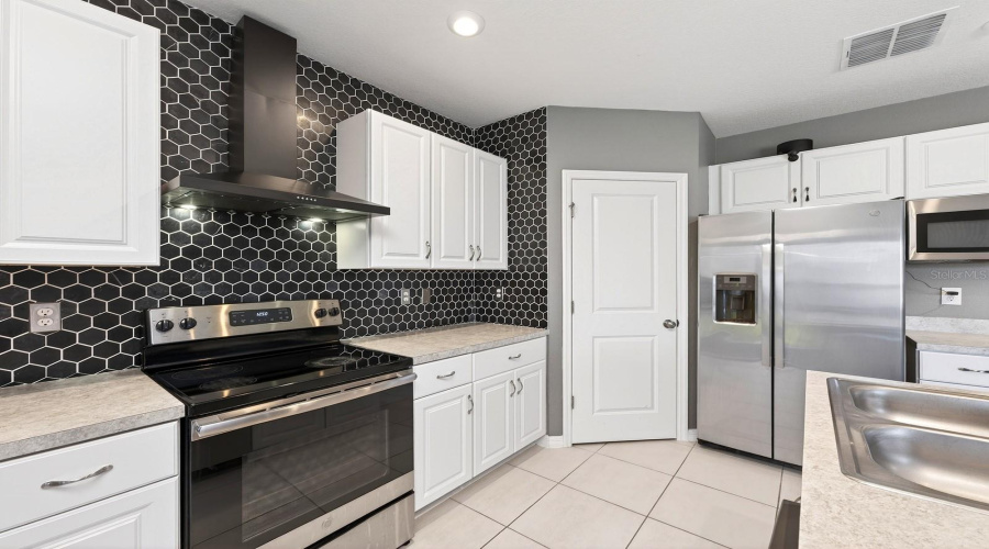 The STYLISH KITCHEN overlooks the main living areas and is thoughtfully designed with white cabinetry, a MODERN STONE BACKSPLASH (2023), stainless steel appliances, a sleek range hood, a Kitchen island with breakfast bar seating, and a walk-in pantry closet.
