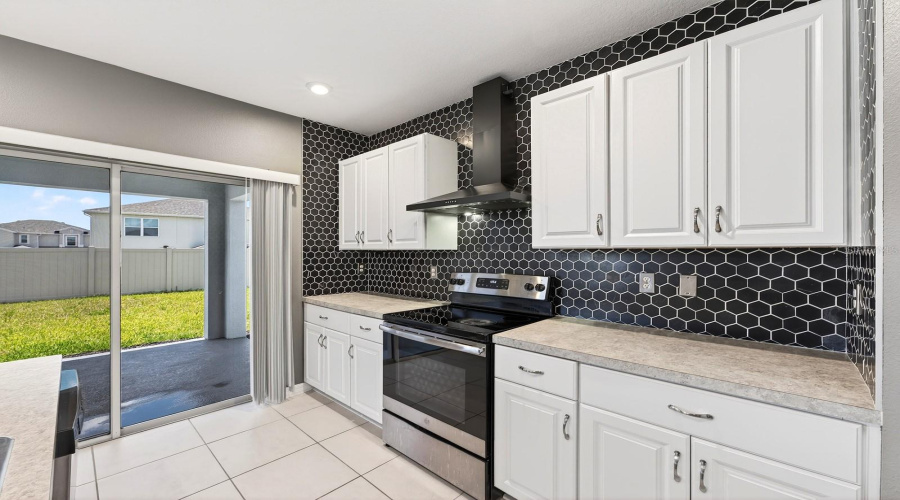 The STYLISH KITCHEN overlooks the main living areas and is thoughtfully designed with white cabinetry, a MODERN STONE BACKSPLASH (2023), stainless steel appliances, a sleek range hood, a Kitchen island with breakfast bar seating, and a walk-in pantry closet.