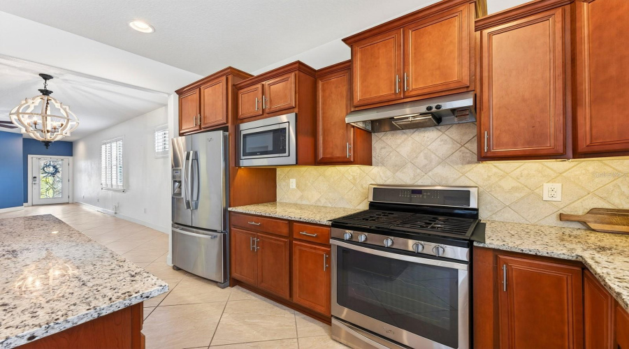Close by is the SPACIOUS KITCHEN, thoughtfully designed with an abundance of cabinetry, granite countertops, UNDER-CABINET LIGHTING, sleek tile backsplash, stainless steel appliances, a center island with counter-height seating, and a closet pantry.