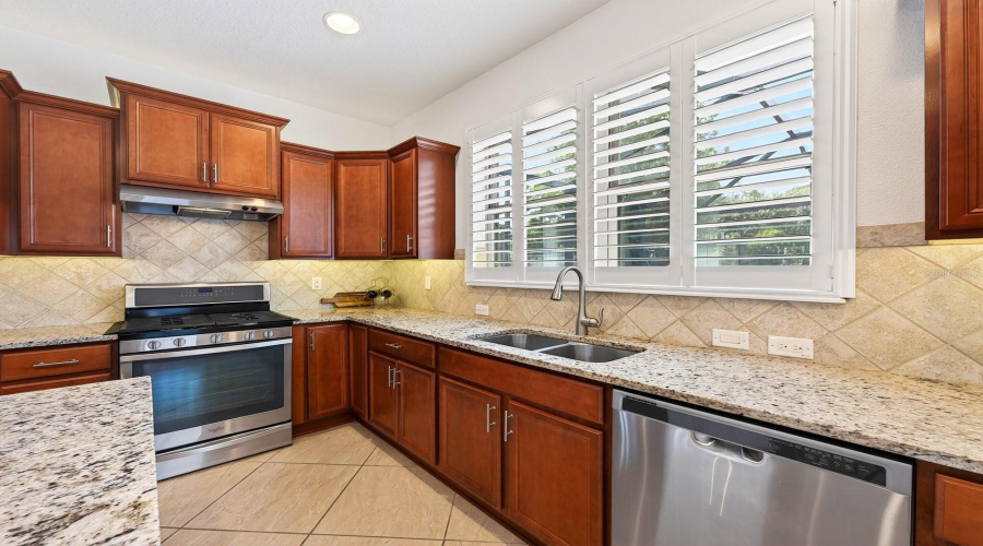 Close by is the SPACIOUS KITCHEN, thoughtfully designed with an abundance of cabinetry, granite countertops, UNDER-CABINET LIGHTING, sleek tile backsplash, stainless steel appliances, a center island with counter-height seating, and a closet pantry.