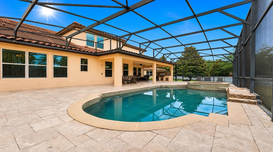 Resort-style covered lanai featuring a fully equipped summer kitchen, ample dining space, and multiple seating areas perfect for year-round outdoor entertaining