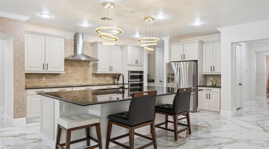 A chef-inspired kitchen featuring white cabinetry, stainless steel appliances, a statement stainless range hood, and an oversized island perfect for cooking, entertaining, and gathering