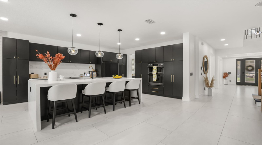 This wide kitchen view highlights the oversized island, built-in appliances, and open connection to the entry and surrounding living spaces.