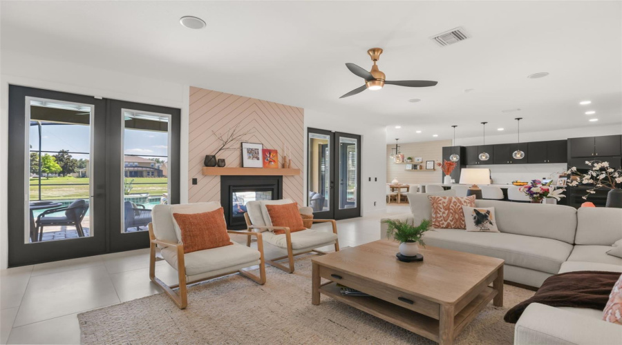 The family room includes a sleek fireplace accent wall, multiple glass doors, and views toward the outdoor living and pool area.