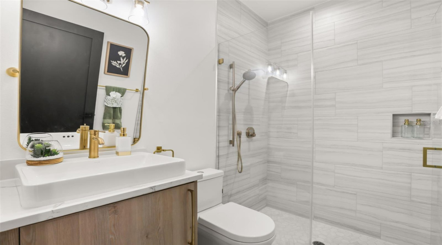 This stylish bath includes a walk-in shower with marble-look tile, brass accents, and a modern vanity with clean finishes.