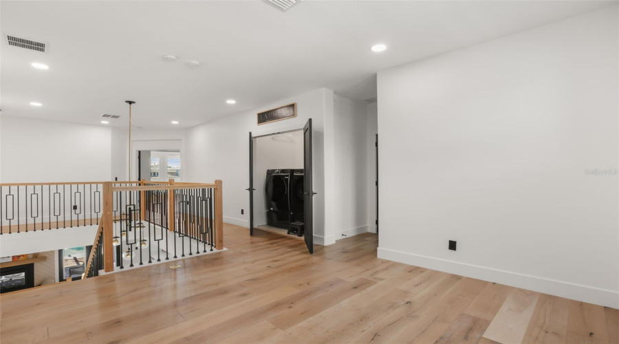 The upstairs landing features warm wood flooring, open railing details, recessed lighting, and convenient access to the laundry area.