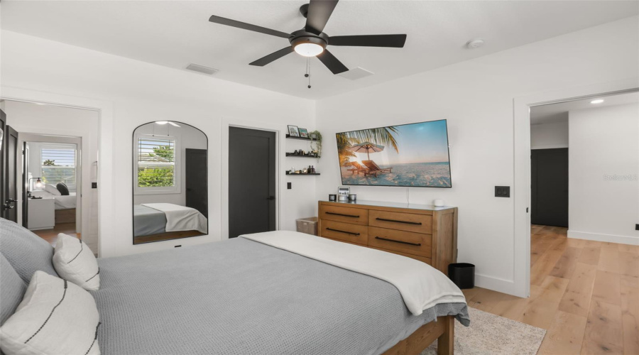A well-sized bedroom features plantation shutters, wood flooring, a ceiling fan, and space for a dresser and media setup.