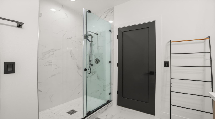 The glass-enclosed shower features marble-look tile, a built-in niche, black trim, and a sleek contemporary design.