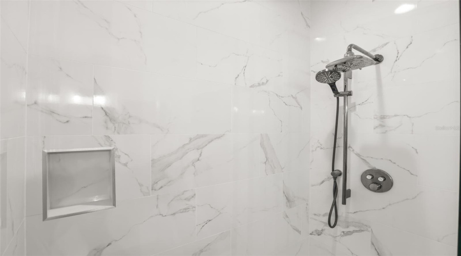 A detailed view highlights the marble-look tile surround, built-in niche, and upgraded shower fixture for a polished finish.