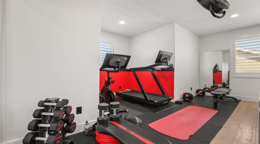 The fitness area includes rubber flooring, cardio equipment, dumbbell storage, and a bold accent wall for an energized workout setup.