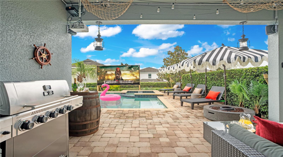 The adventure continues outdoors. The covered lanai features mounted outdoor speakers, an outdoor grill, comfortable lounge seating, lighting, a fire pit and views of outdoor movie projector and the private resort-style backyard.