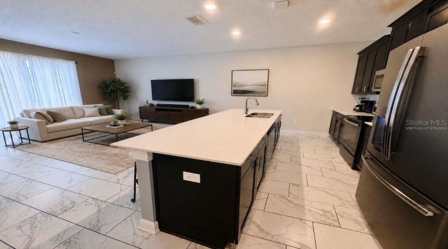 Virtually staged kitchen and living area highlighting the large center island, open layout, and comfortable flow for guests and everyday living.