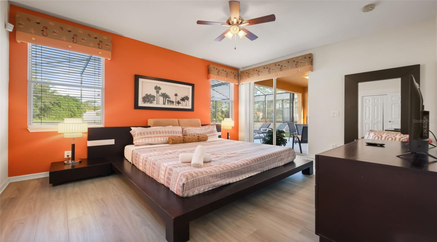 Spacious primary suite featuring a king-size bed, vaulted ceiling, and sliding glass doors opening directly to the pool deck.